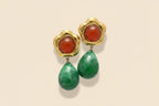 Gold earrings with red and green stones on a beige background