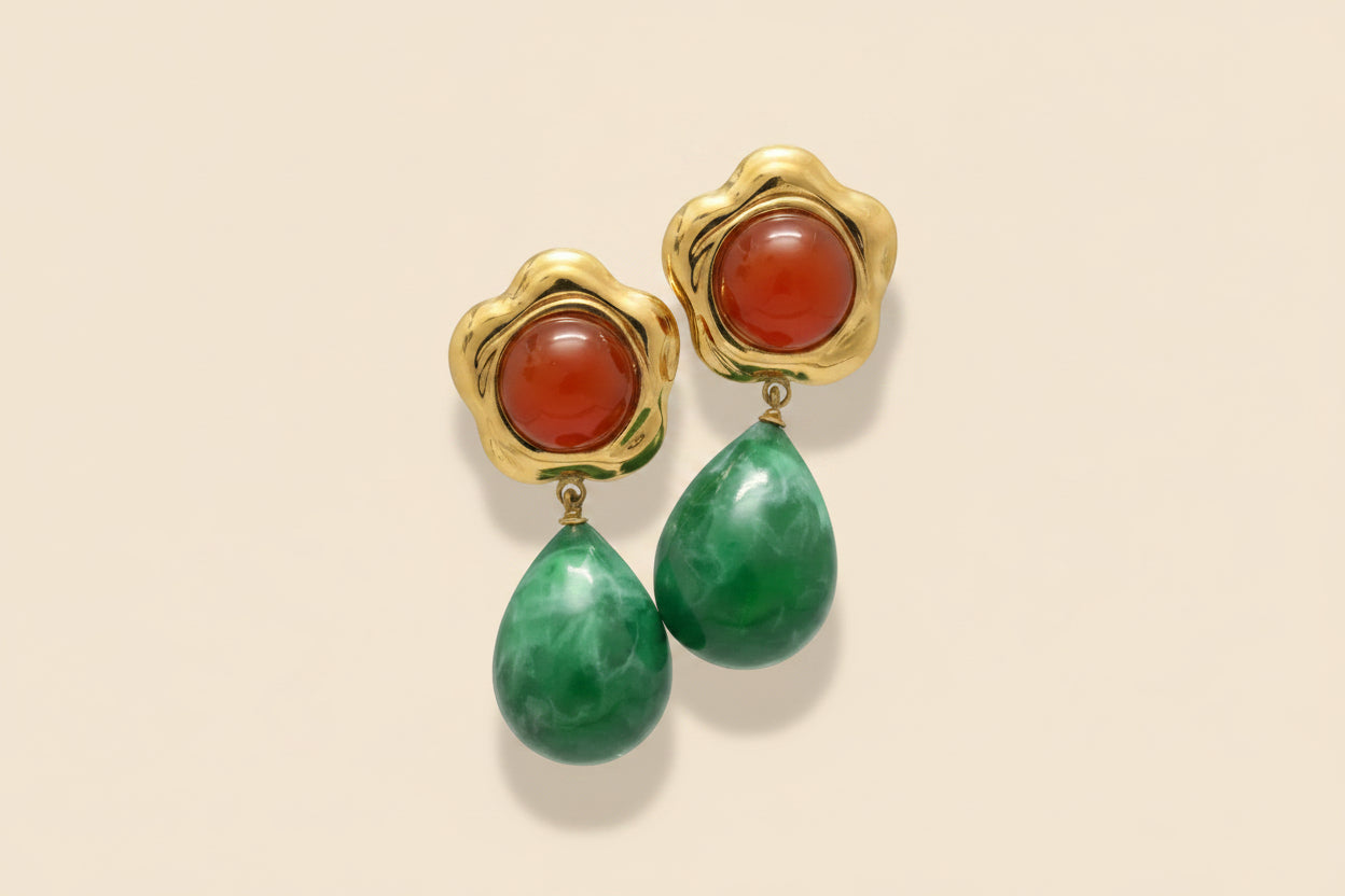 Gold earrings with red and green stones on a beige background