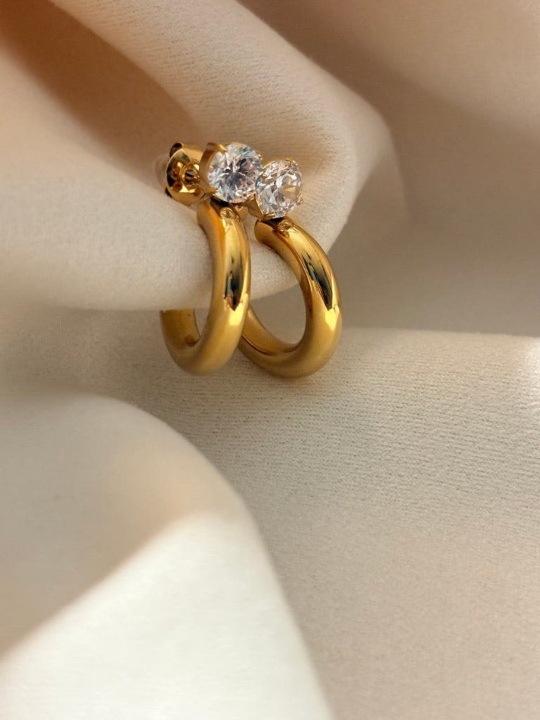 Gold hoop earrings with zircon stones on a beige background.