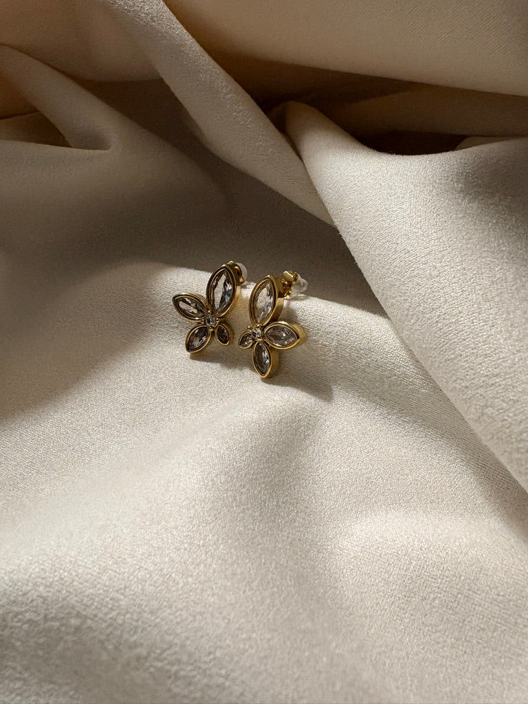 Zircon petal earrings on a soft beige fabric.