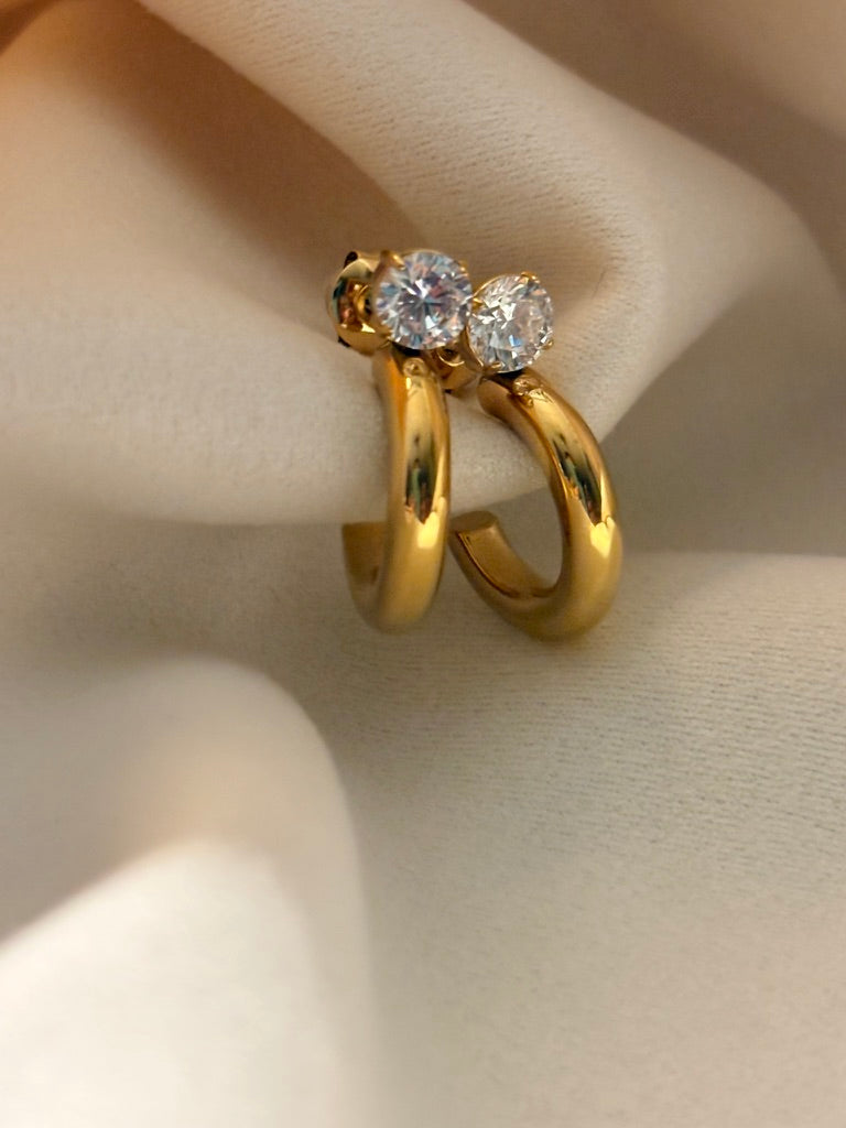 Gold hoop earrings with diamond-like stones on a neutral background.