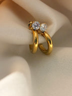 Gold hoop earrings with diamond-like stones on a neutral background.