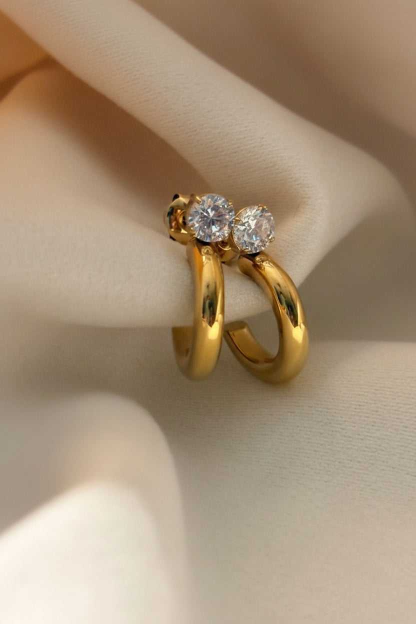 Gold hoop earrings with diamond-like stones on a neutral background.