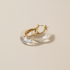 Gold hoop earrings with clear stones on a soft fabric background