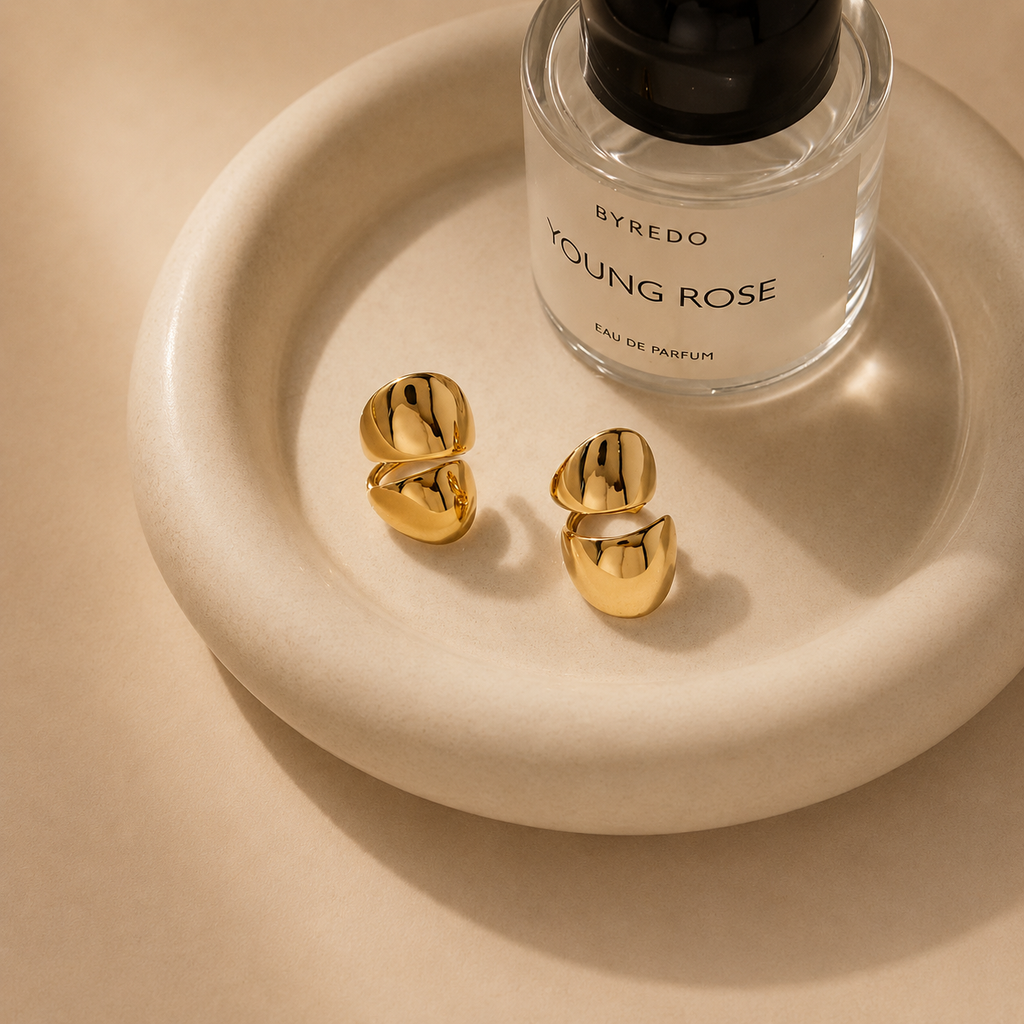 Gold earrings and a perfume bottle on a white display tray by NIYANSA