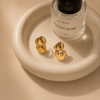 Gold earrings and a perfume bottle on a white display tray by NIYANSA