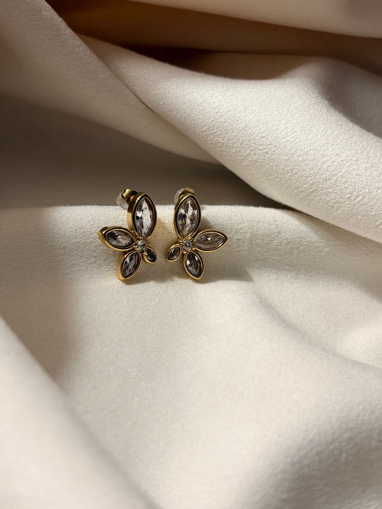 Flower-shaped earrings with zirconia stones on a soft white fabric background