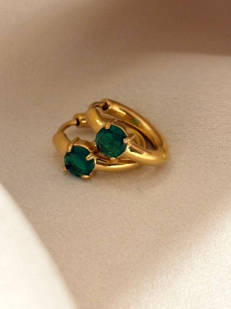 18kt gold plated earrings with two green CZ gemstones on a beige background.