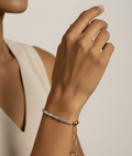 Woman wearing an adjustable gold-tone tennis bracelet featuring a row of round brilliant-cut cubic zirconia stones. The bracelet is styled on the wrist against a off white background, highlighting its delicate sparkle, sliding clasp closure, and elegant everyday wear design.