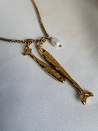 18kt PVD Coated gold necklace with fish-shaped pendants on a light fabric background by NIYANSA.