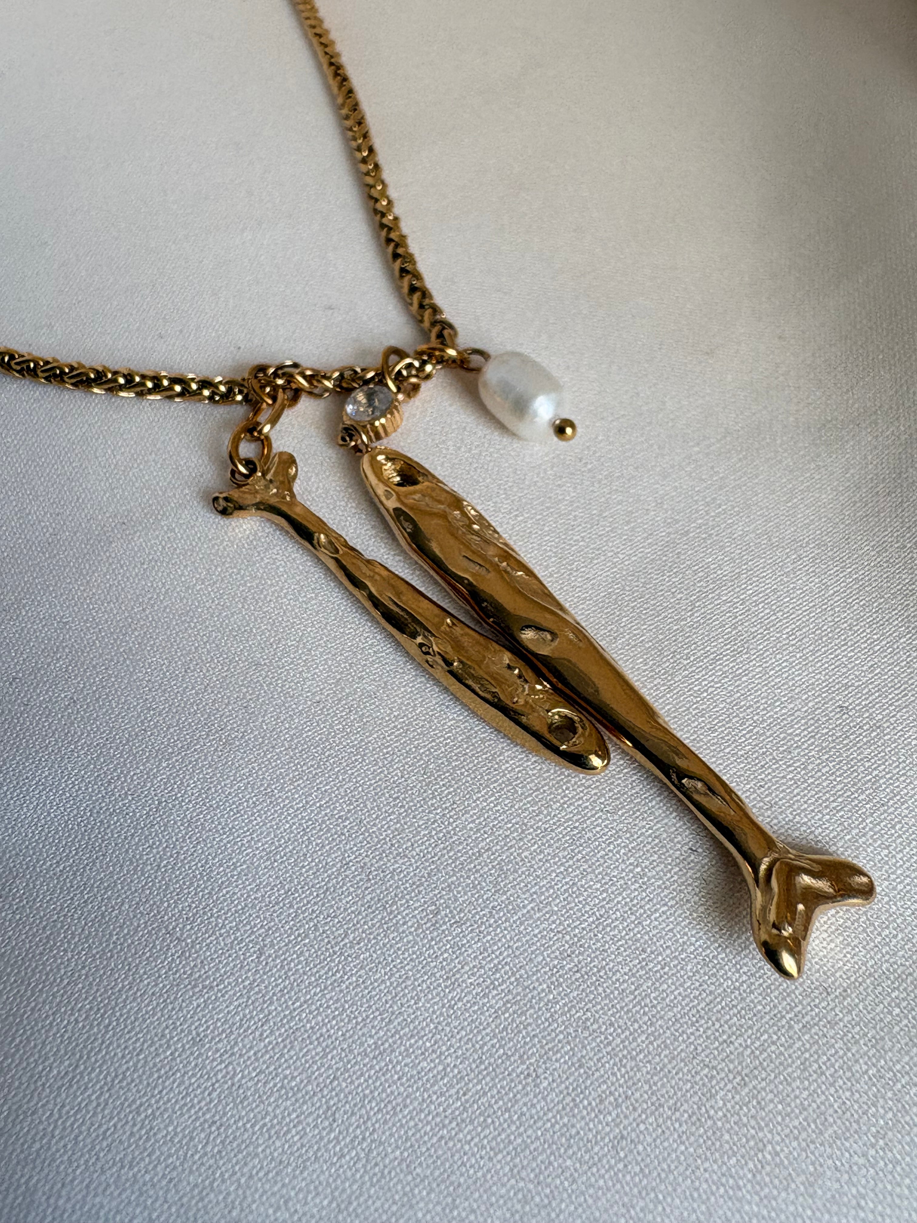 18kt PVD Coated gold necklace with fish-shaped pendants on a light fabric background by NIYANSA.