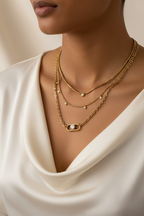 Model wearing a layered gold necklace featuring mixed chain textures, delicate AAA cubic zirconia accents, and a statement clasp pendant in 18KT PVD gold-plated stainless steel by NIYANSA.