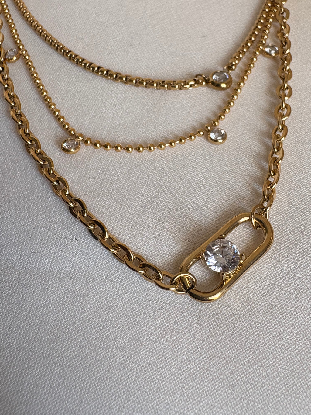 Close-up of a layered gold necklace featuring mixed chain textures, bezel-set AAA cubic zirconia accents, and a statement clasp pendant with a solitaire cubic zirconia stone, crafted in 18KT PVD gold-plated stainless steel by NIYANSA.