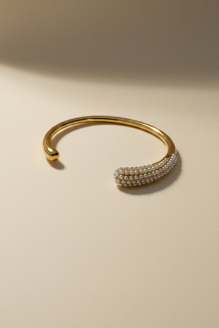 Gold bracelet with pearl-like beads on a light beige background