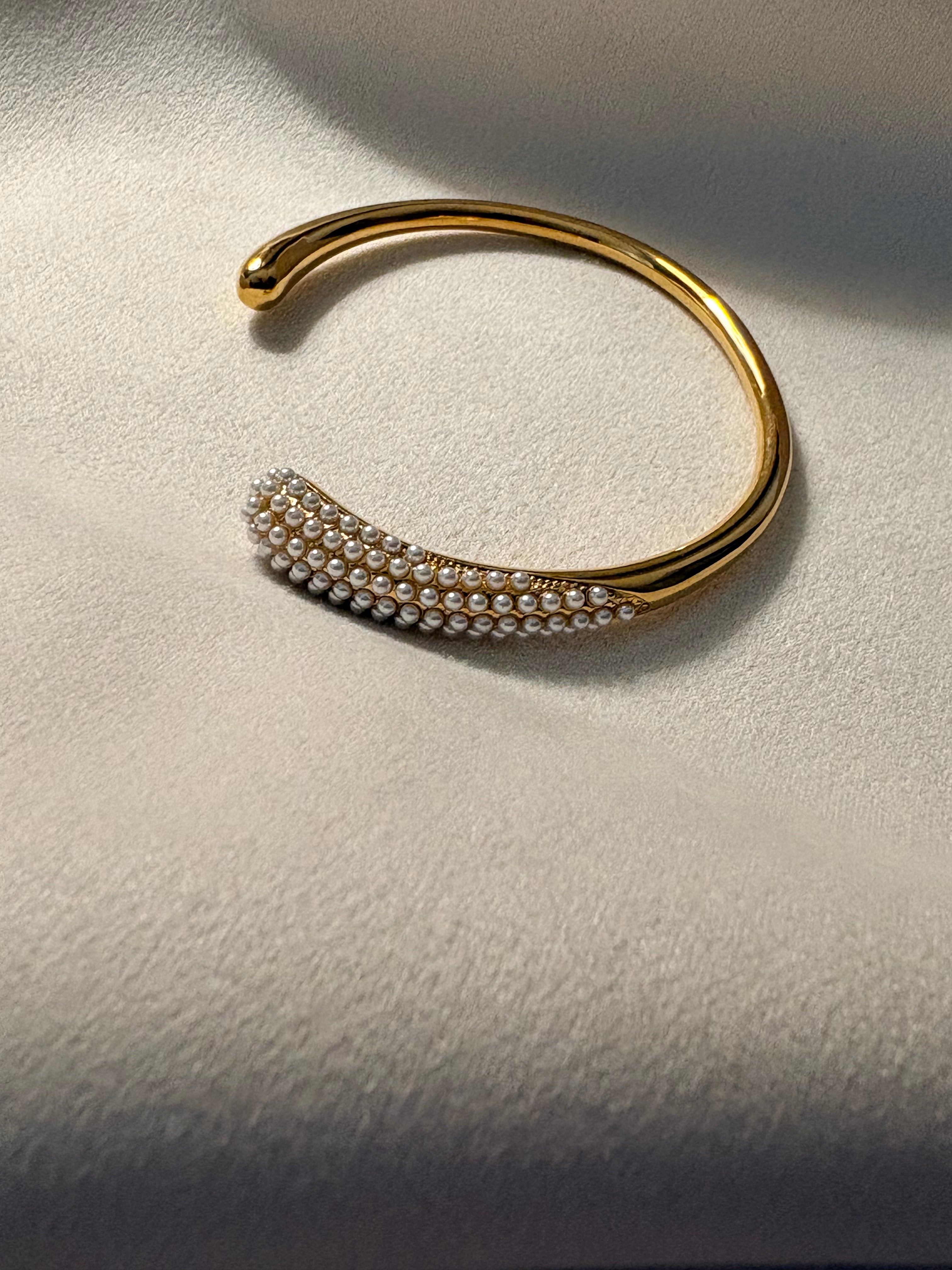 Gold bracelet with pearl-like beads on a textured surface