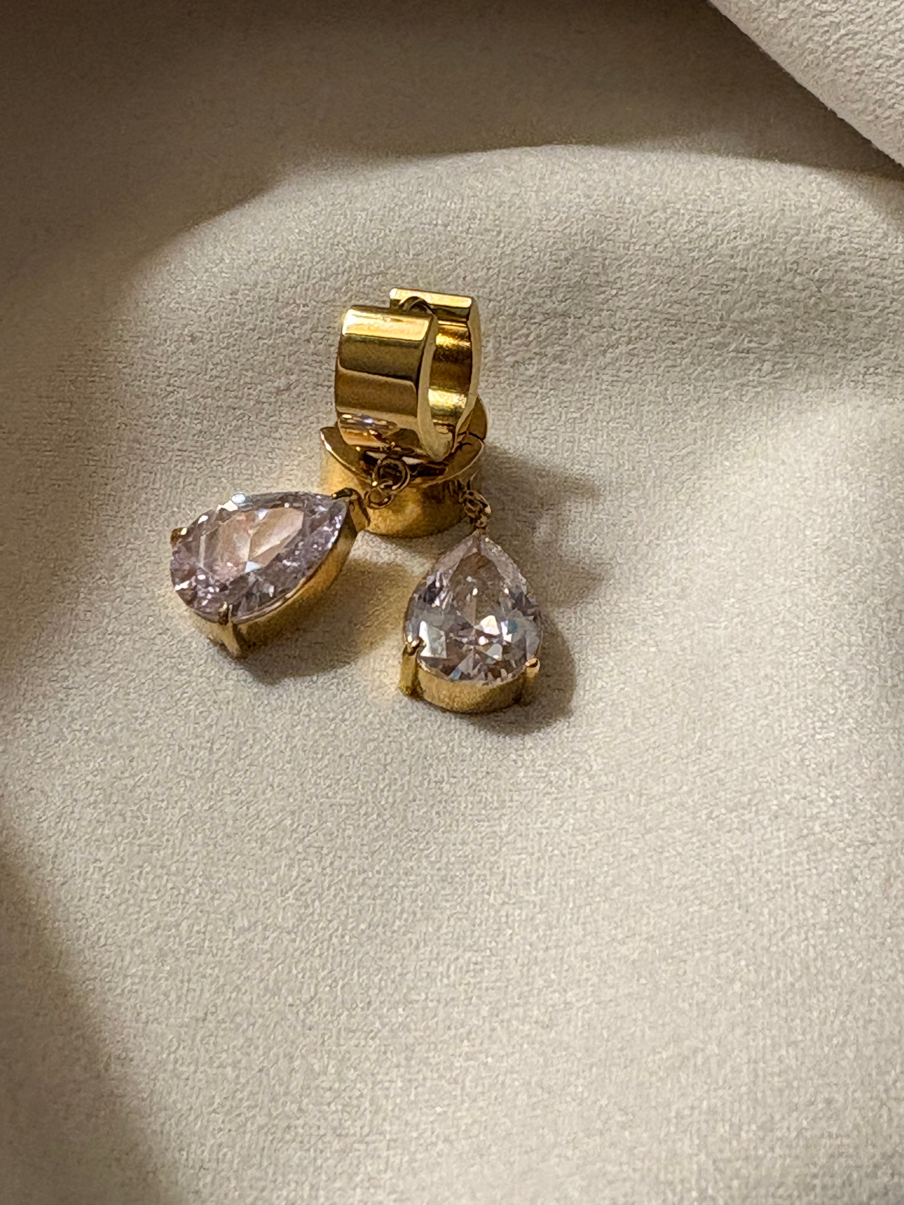 Gold earrings with teardrop-shaped CZ  stones on a light background.