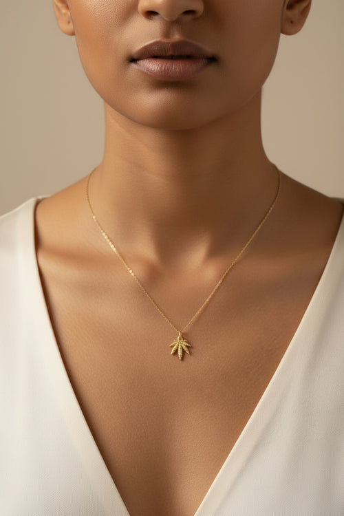 Gold charm shaped like a palm tree on a light beige background