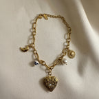 18kt pvd Gold bracelet with heart-shaped charm and various other charms on a beige background