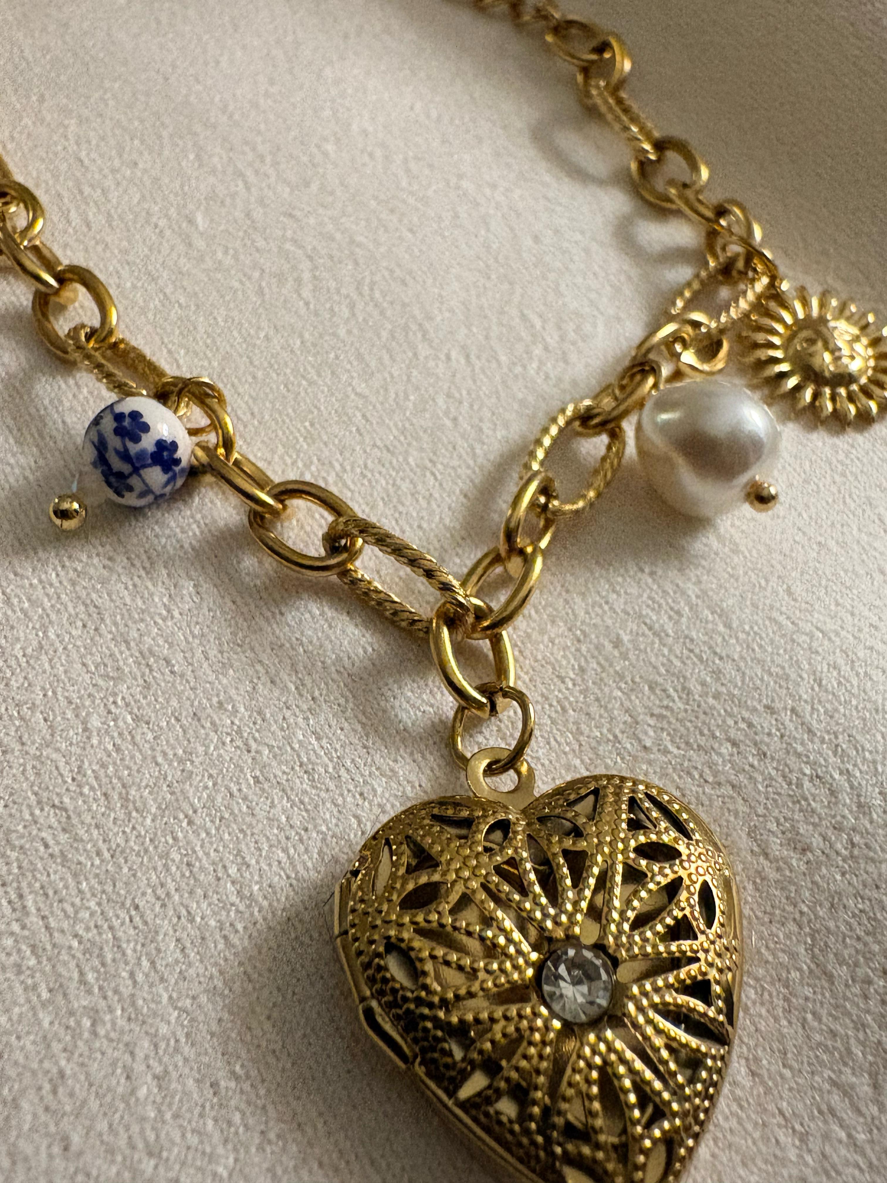 18kt gold chain bracelet with heart-shaped locket and decorative beads on a light background