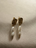 Pair of 18kt gold plated freshwater pearl earrings on a beige surface