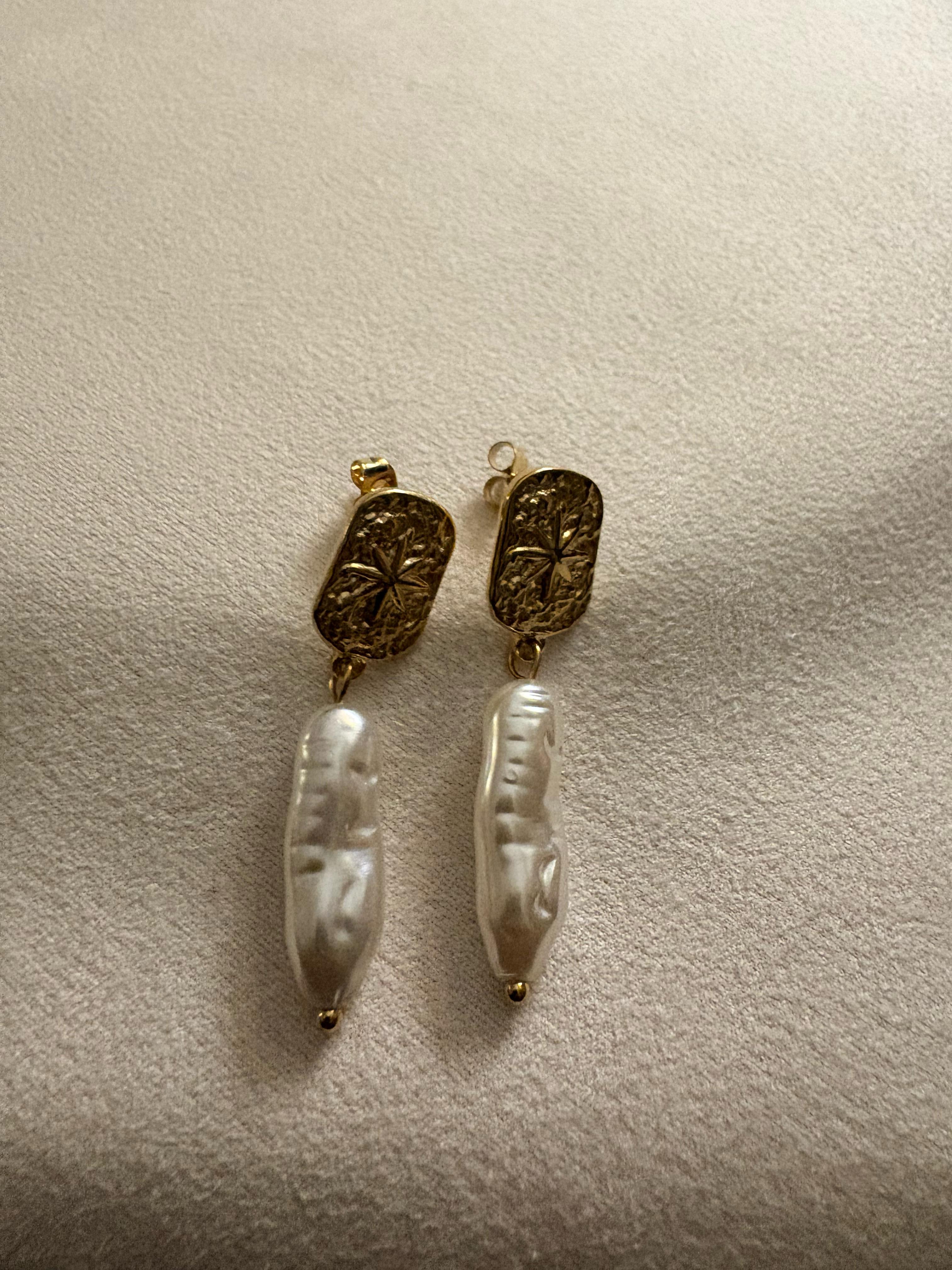 Pair of 18kt gold plated freshwater pearl earrings on a beige surface